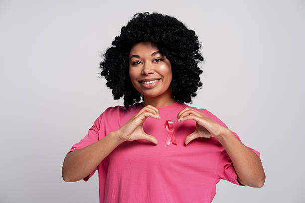 Smiling woman wearing pink t-shirt making heart shape with hands supporting breast cancer awareness campaign